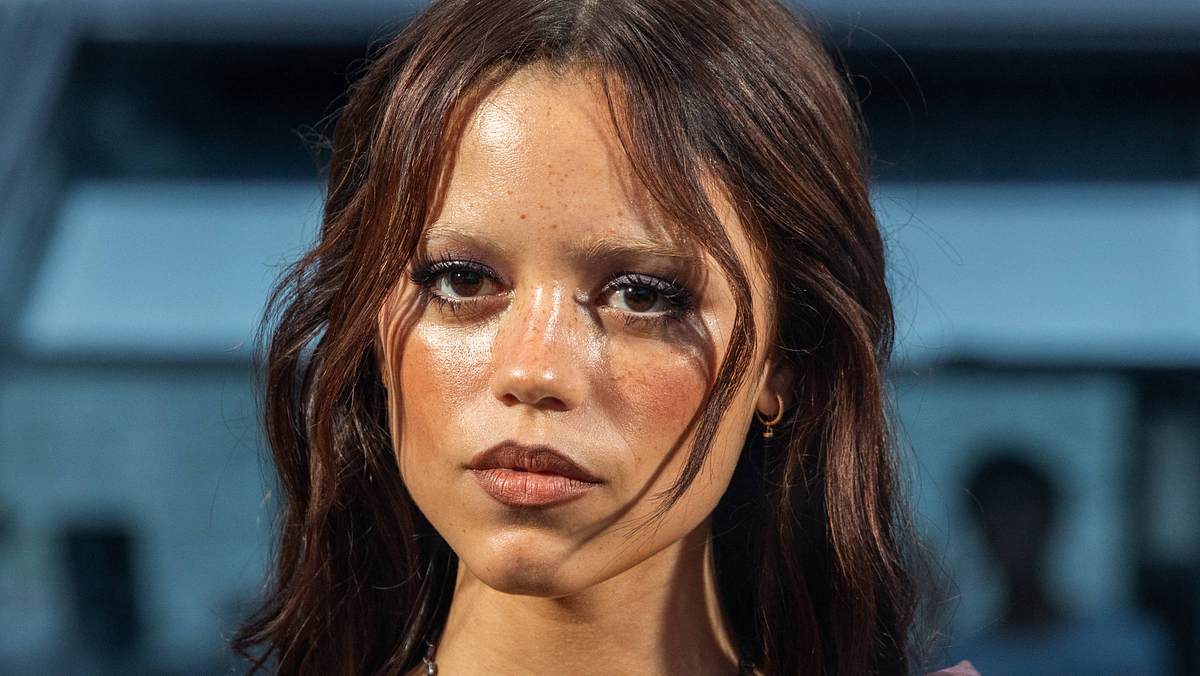 Jenna Ortega ist einer der größten Serien-Stars der jungen Generation. Jenna Ortega mit starkem Make-up und roten Haaren schaut ernst in die Ferne.