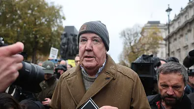 Jeremy Clarkson mit Mütze und braunem Mantel, umringt von Kameras und Fotografen. - Foto: IMAGO / i Images Jeremy Clarkson mit Mütze und braunem Mantel, umringt von Kameras und Fotografen. - Foto: IMAGO / i Images