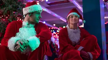 Olivia Holt und Connor Swindells sitzen nebeneinander in Weihnachtsmann-Kostümen aus „Jingle Bell Heist“. - Foto: Netflix