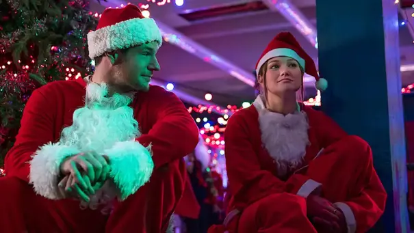 Olivia Holt und Connor Swindells sitzen nebeneinander in Weihnachtsmann-Kostümen aus „Jingle Bell Heist“. - Foto: Netflix