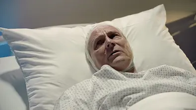 Jo Gerner liegt mit ängstlichem Gesicht und Bandage um den Kopf im Bett. - Foto: RTL