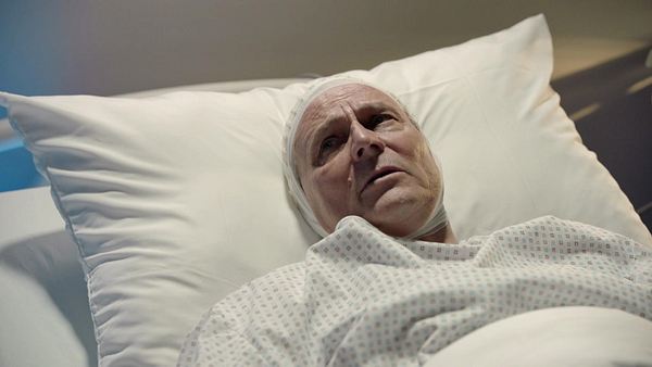 Jo Gerner liegt mit ängstlichem Gesicht und Bandage um den Kopf im Bett. - Foto: RTL