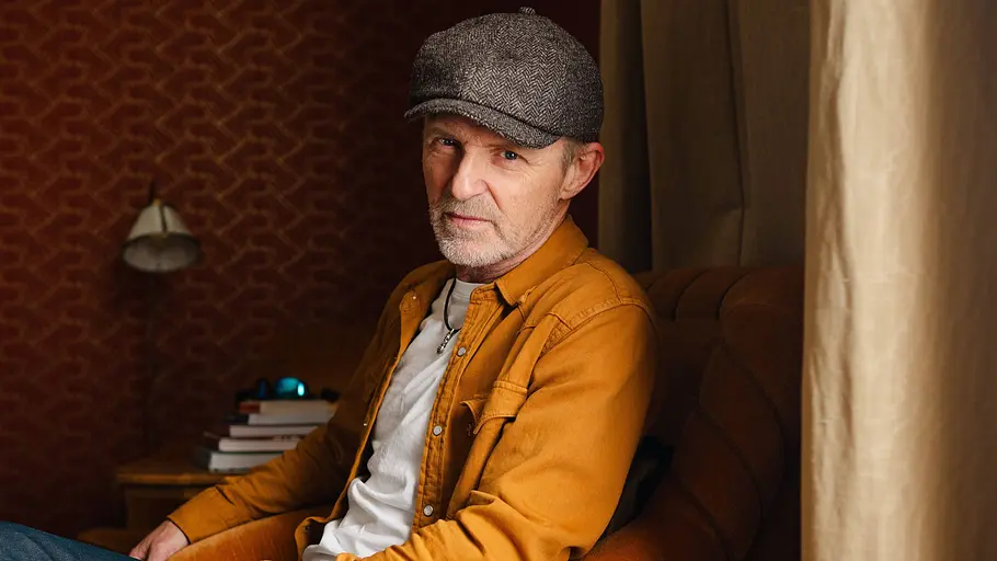 Ein Porträt von Autor Jo Nesbø, der mit orangener Jacke und Kappe ernst zur Kamera schaut