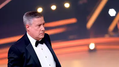 Joachim Llambi trägt einen schwarzen Smoking mit Fliege und blickt nach rechts. Im Hintergrund leuchten orange Lichtstreifen. - Foto: IMAGO / Panama Pictures Joachim Llambi trägt einen schwarzen Smoking mit Fliege und blickt nach rechts. Im Hintergrund leuchten orange Lichtstreifen. - Foto: IMAGO / Panama Pictures