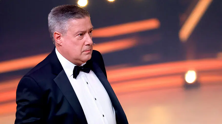 Joachim Llambi in tiefer Trauer: „Manchmal fehlen einfach die Worte“ Joachim Llambi trägt einen schwarzen Smoking mit Fliege und blickt nach rechts. Im Hintergrund leuchten orange Lichtstreifen.