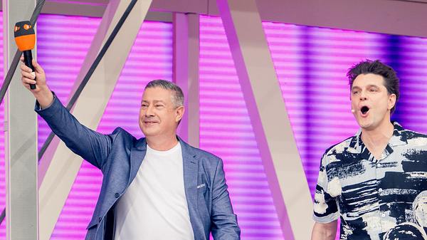 Joachim Llambi und Lutz van der Horst begrüßen das „ZDF Fernsehgarten“-Publikum. Llambi streckt seinen rechten Arm in die Luft, in der Hand hält er ein ZDF-Mikrofon. - Foto: ZDF/Maximilian von Lachner