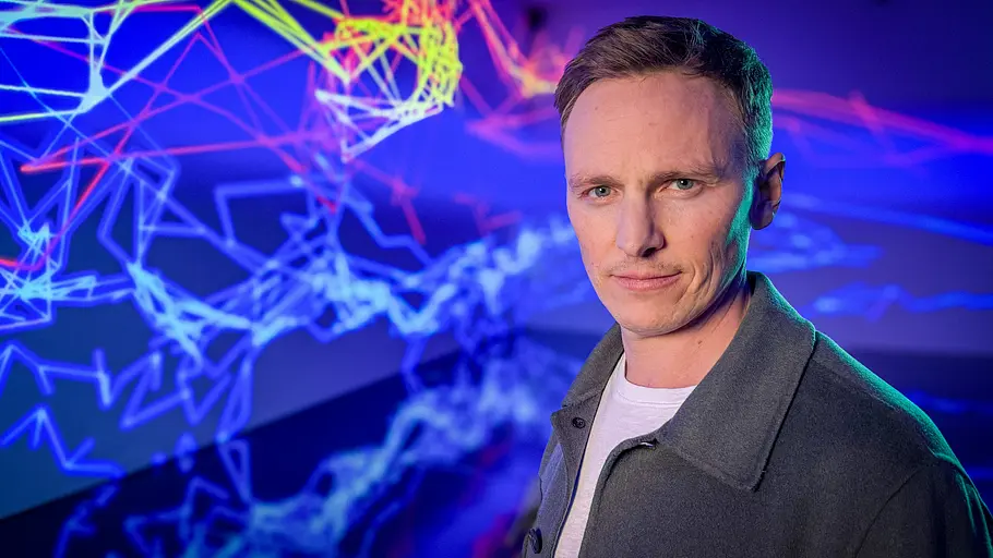 Jochen Breyer führt durch die Dokumentation und reist für seine Recherchen bis in die USA. Die Wahrheit über Social Media - mit Jochen Breyer: Jochen Breyer steht vor einer Projektion mit Linien und schaut in die Kamera.