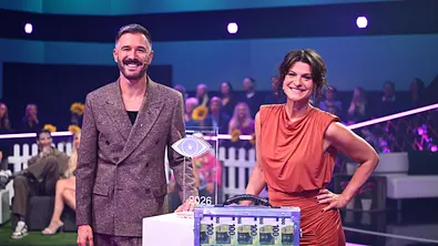 Jochen Schropp und Marlene Lufen stehen lächelnd neben einer Trophäe und einem transparenten Koffer mit 100-Euro-Scheinen. - Foto: Joyn/Willi Weber Jochen Schropp und Marlene Lufen stehen lächelnd neben einer Trophäe und einem transparenten Koffer mit 100-Euro-Scheinen. - Foto: Joyn/Willi Weber