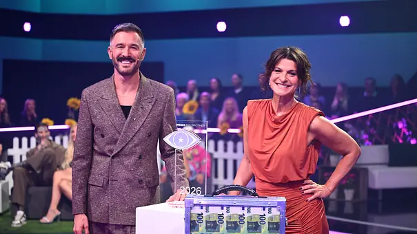 Jochen Schropp und Marlene Lufen stehen lächelnd neben einer Trophäe und einem transparenten Koffer mit 100-Euro-Scheinen. - Foto: Joyn/Willi Weber Jochen Schropp und Marlene Lufen stehen lächelnd neben einer Trophäe und einem transparenten Koffer mit 100-Euro-Scheinen. - Foto: Joyn/Willi Weber