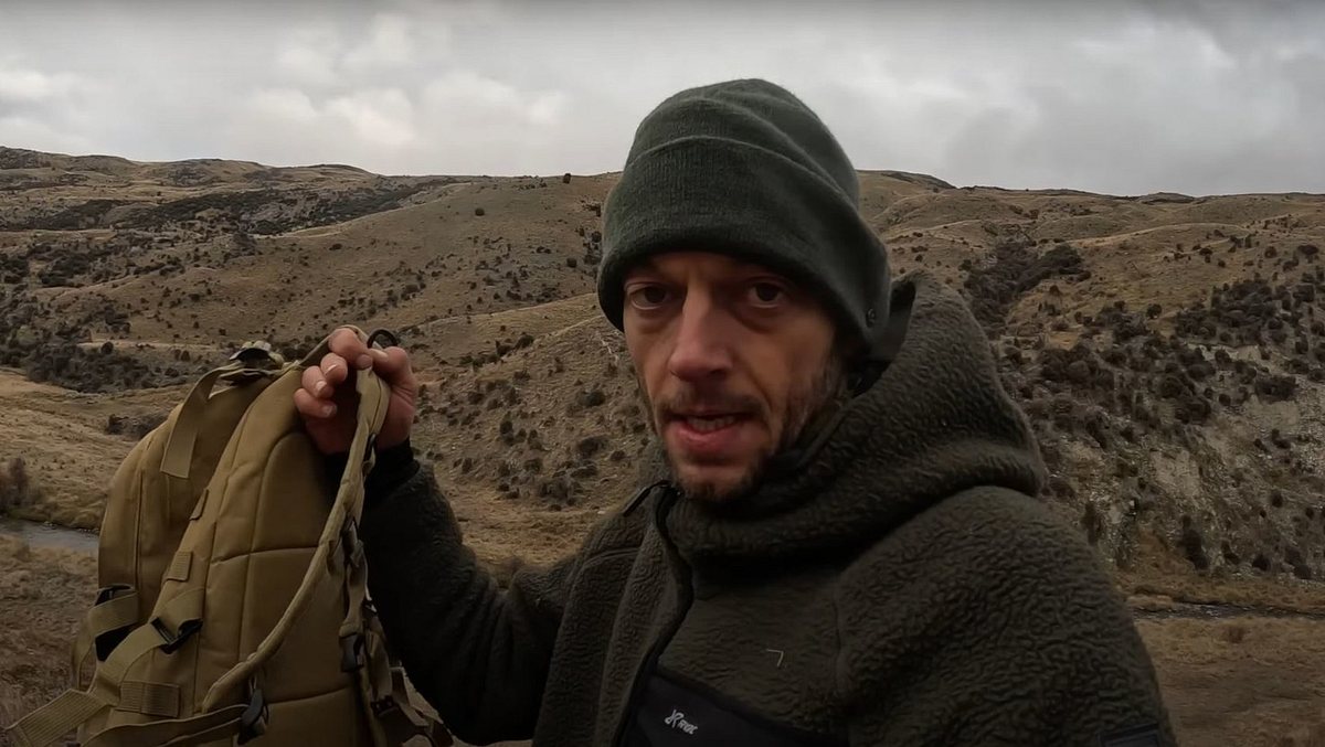 Joe Vogel erzählt endlich seine Version der Wahrheit. Joe Vogel schaut in die Kamera und hält seinen Rucksack hoch.