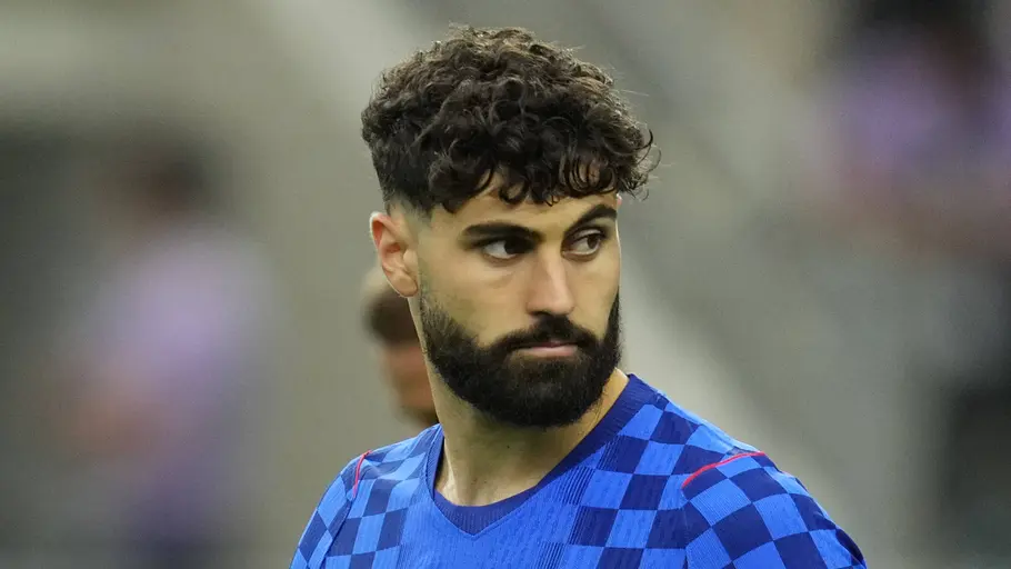 Fußballspieler im blau karierten Trikot der kroatischen Nationalmannschaft blickt während des Aufwärmens konzentriert zur Seite. Im Hintergrund ist das Stadion unscharf zu erkennen.
