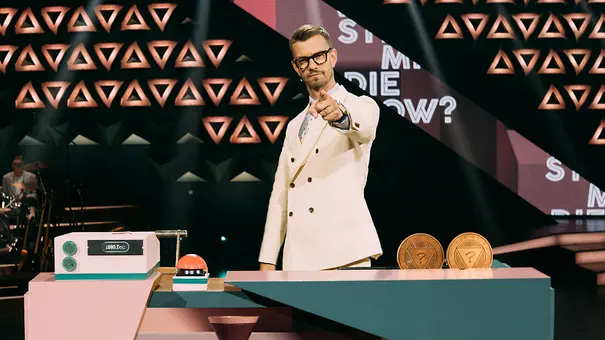 Joko Winterscheidt steht ernst am Moderationspult und zeigt mit dem Zeigefinger in die Kamerain der ProSieben-Show „Wer stiehlt mir die Show?“ und bereitet sich auf die nächste Runde mit seinen prominenten Gästen vor. - Foto: Seven.One/Florida