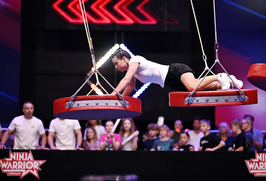 Josie Frank ist Teilnehmerin bei Ninja Warrior Germany 2026 Josie Frank stützt sich bei „Ninja Warrior Germany“ auf zwei rote, an Seilen hängende Plattformen. Dahinter steht Publikum.