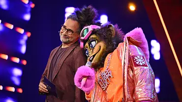 Matthias Opdenhövel mit Brille steht auf einer Bühne neben Three Sixty im pelzigen Tierkostüm mit orange-pinker Glitzerjacke und Mikrofon. - Foto: Joyn/Willi Weber Matthias Opdenhövel mit Brille steht auf einer Bühne neben Three Sixty im pelzigen Tierkostüm mit orange-pinker Glitzerjacke und Mikrofon. - Foto: Joyn/Willi Weber