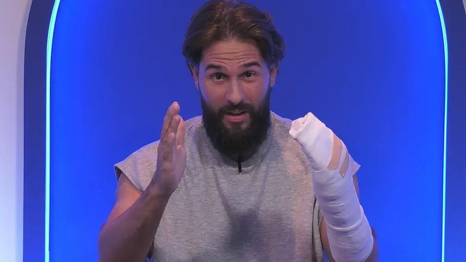 Maurice Dziwak Promi Big Brother Verletzung Maurice Dziwak im grauen ärmellosen Shirt gestikuliert vor blauem Hintergrund. Eine Hand und ein Unterarm sind weiß bandagiert.