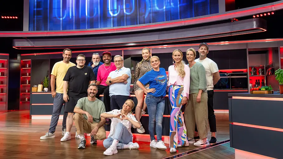 Promi Taste Kandidat:innen Die Kandidatinnen und Kandidaten von „Promi Taste“ stehen gemeinsam im Studio vor dem großen „The Taste“-Logo und lächeln in die Kamera.