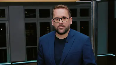 Paul Ronzheimer steht in einem TV-Studio vor beleuchtetem „Ronzheimer“-Schriftzug. - Foto: SAT.1 / Joyn / Christoph Köstlin