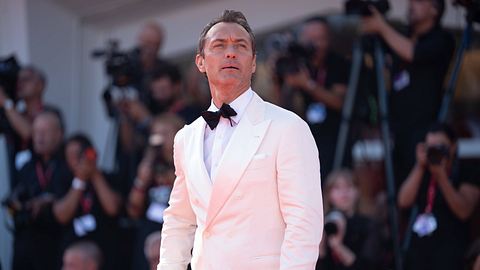 Jude Law im weißen Smoking auf dem roten Teppich der Filmfestspiele von Venedig. Er trägt eine schwarze Krawatte, im Hintergrund fotografiert ihn die Presse.  - Foto: IMAGO / NurPhoto