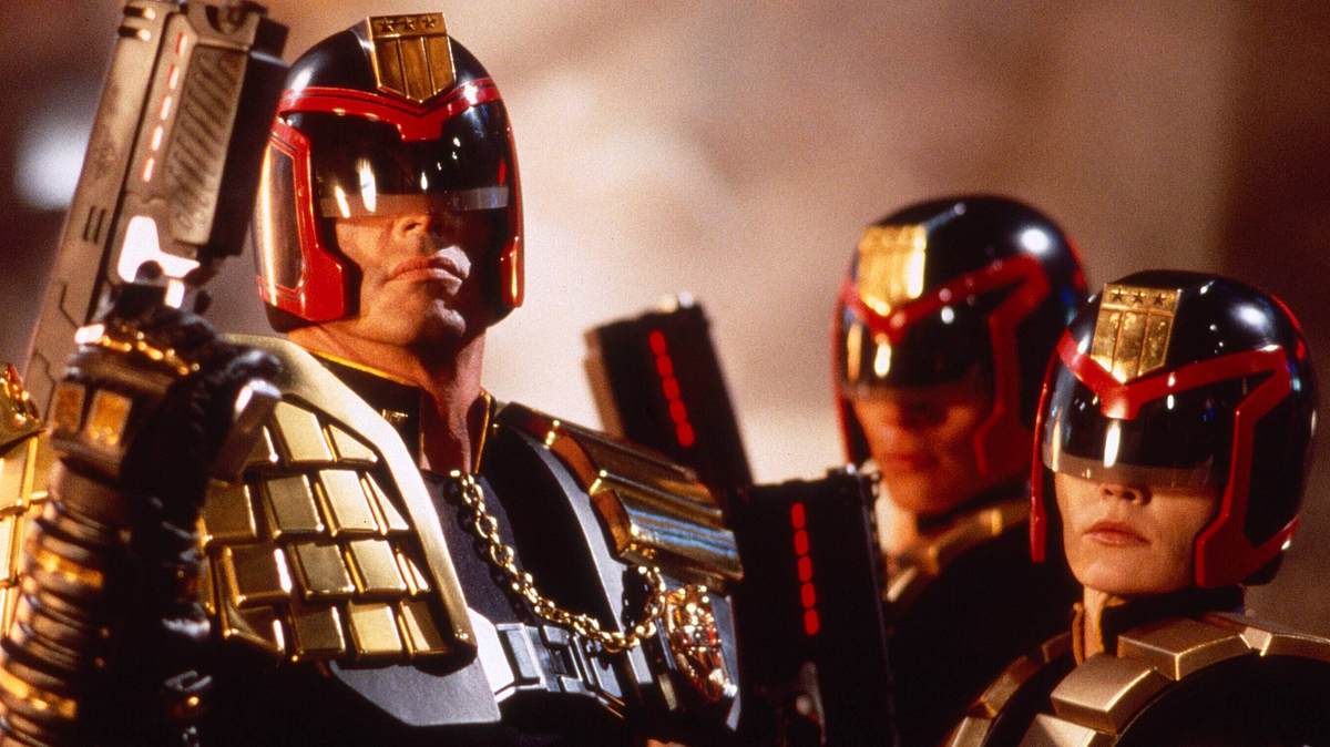 Man sieht „Judges“ aus „Judge Dredd“ von 1995. Links steckt Sylvester Stallone unter einem rot-schwarzen Helm mit Blende vor den Augen. Dazu kommt eine goldene Weste und eine Waffe in ähnlicher rot-schwarz Optik. Die anderen beiden Judges rechts von Stallone sehen ebenso aus.