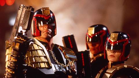 Man sieht „Judges“ aus „Judge Dredd“ von 1995. Links steckt Sylvester Stallone unter einem rot-schwarzen Helm mit Blende vor den Augen. Dazu kommt eine goldene Weste und eine Waffe in ähnlicher rot-schwarz Optik. Die anderen beiden Judges rechts von Stallone sehen ebenso aus. - Foto:  IMAGO / Everett Collection