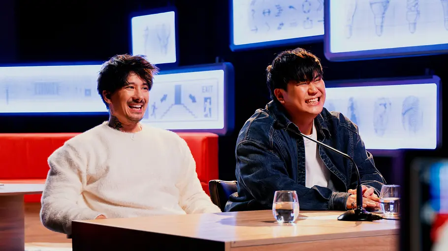 Julien Bam (links) und Joon Kim (rechts) sitzen an einem Schreibtisch. Sie moderieren Staffel 2 von „The Way Out“.
