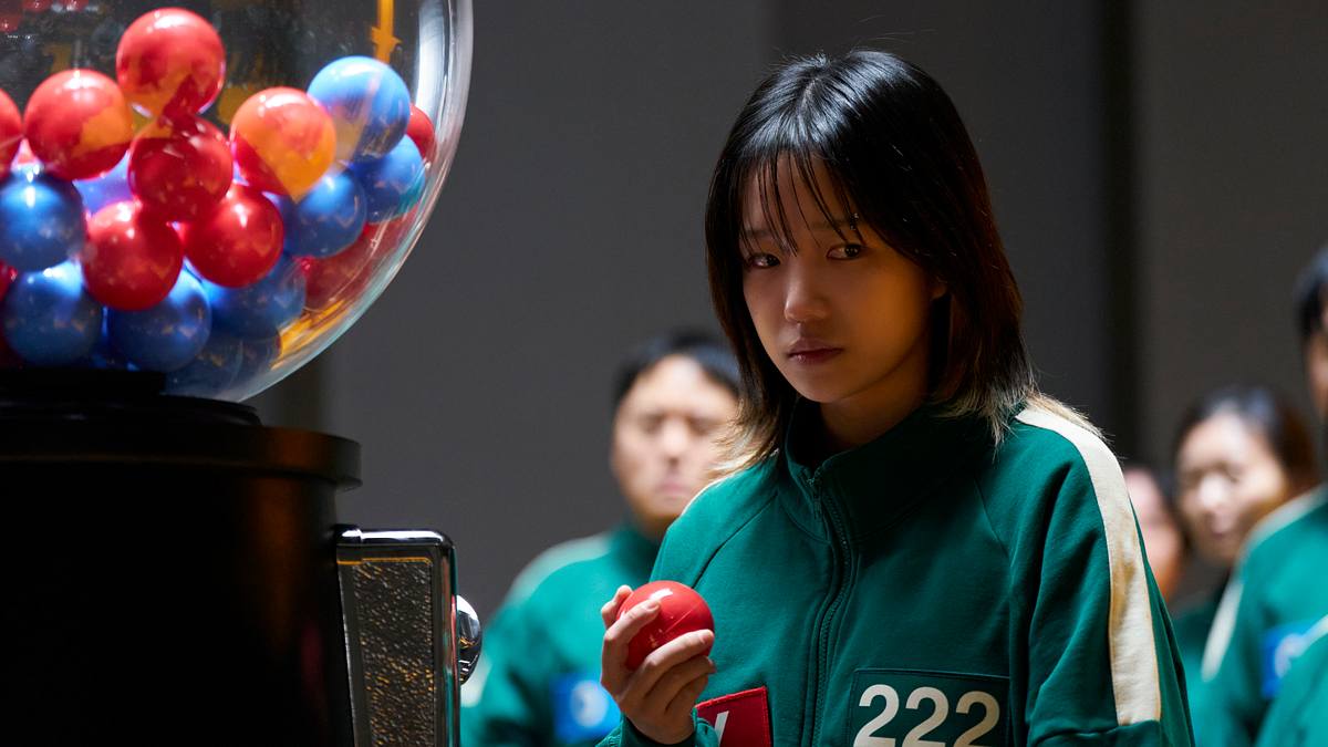 Jun-hee ist nicht gerade in der besten Verfassung für tödliche Spiele. Jun-hee hält einen roten ball in der rechten Hand und schaut nachdenklich zur Seite.