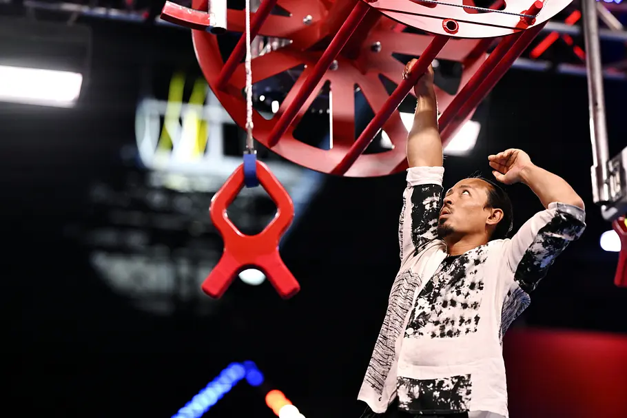 Jun Kim ist Teilnehmer bei Ninja Warrior Germany 2026 Jun Kim hält sich mit einer Hand an einer roten Stange fest und blickt nach oben. Neben ihm hängt ein roter Griff.