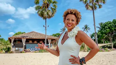 Arabella Kiesbauer steht für „Reality AllStars“ in einem weißen Kleid auf einem Strand und lächelt. - Foto: RTL2 Arabella Kiesbauer steht für „Reality AllStars“ in einem weißen Kleid auf einem Strand und lächelt. - Foto: RTL2
