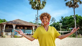 Moderatorin Arabella Kiesbauer steht lächelnd am Star-Strand von KDRS in Thailand, trägt ein gelbes Kleid und breitet einladend die Arme aus, Palmen und Strandkulisse im Hintergrund. - Foto: RTLZWEI - Luis Zeno Kuhn Moderatorin Arabella Kiesbauer steht lächelnd am Star-Strand von KDRS in Thailand, trägt ein gelbes Kleid und breitet einladend die Arme aus, Palmen und Strandkulisse im Hintergrund. - Foto: RTLZWEI - Luis Zeno Kuhn