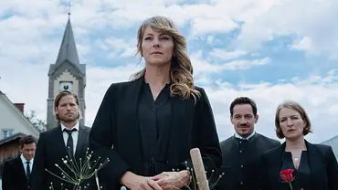 Katharina steht in schwarzer Kleidung vor einem Blumengesteck. Hinter ihr stehen Markus, Tobi und seine Frau, rechts mit Rosen, und ein Kirchturm. - Foto: ZDF/Sabine Finger Fotografie Katharina steht in schwarzer Kleidung vor einem Blumengesteck. Hinter ihr stehen Markus, Tobi und seine Frau, rechts mit Rosen, und ein Kirchturm. - Foto: ZDF/Sabine Finger Fotografie
