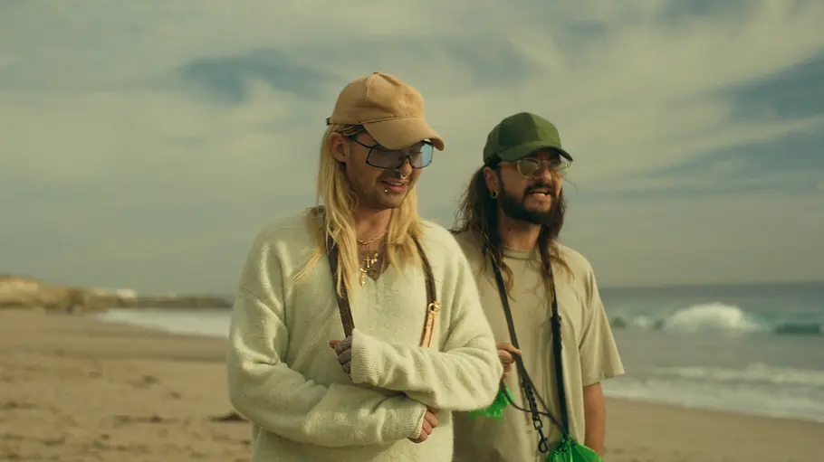Bill und Tom Kaulitz laufen mit Kappe und Sonnenbrille am Strand entlang.