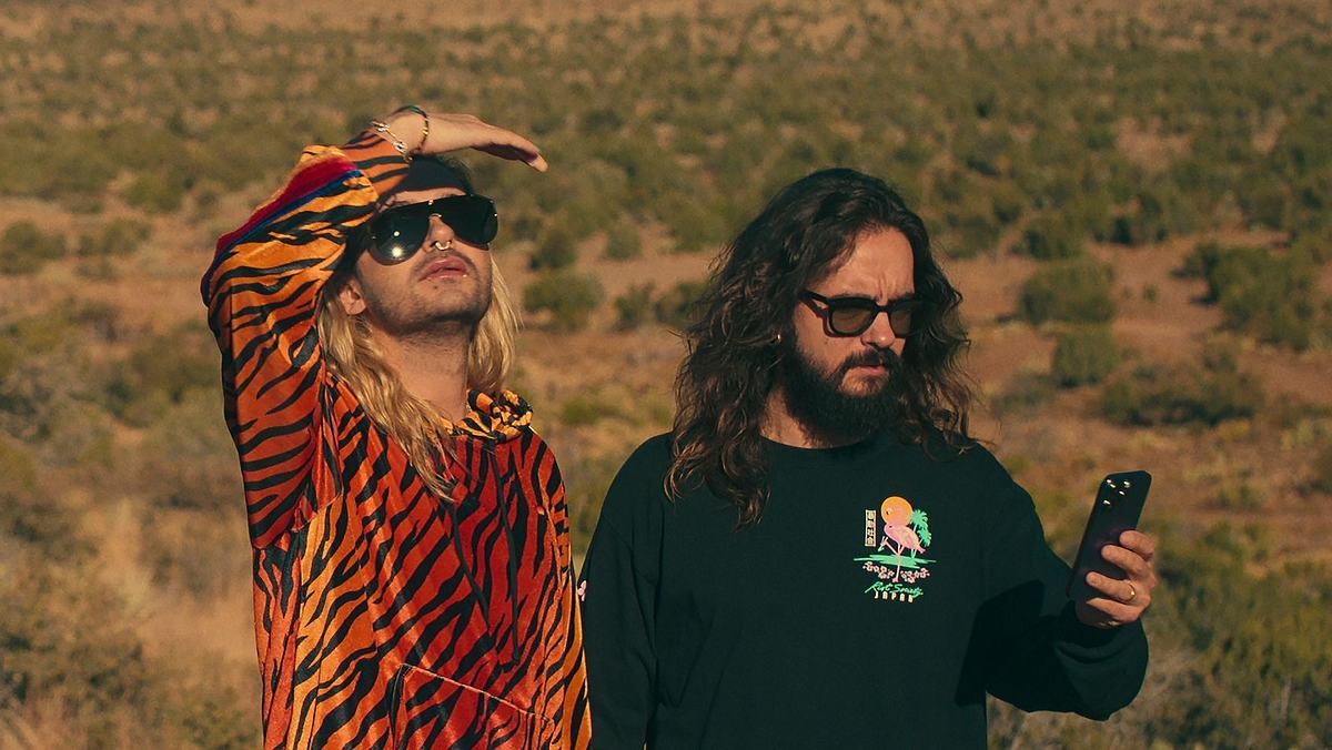 Enthüllung nach „Kaulitz & Kaulitz“, Staffel 2 Szene aus „Kaulitz & Kaulitz“: Bill Kaulitz trägt einen Jogginganzug mit Tiger-Print und schaut in die Ferne, Tom Kaulitz guckt verwirrt auf sein Handy