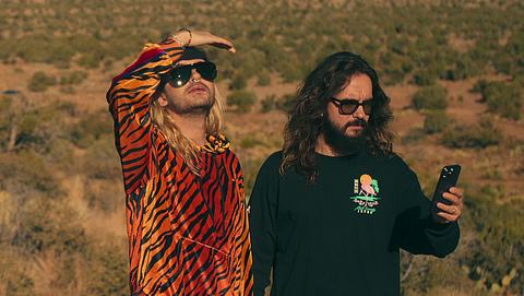 Szene aus „Kaulitz & Kaulitz“: Bill Kaulitz trägt einen Jogginganzug mit Tiger-Print und schaut in die Ferne, Tom Kaulitz guckt verwirrt auf sein Handy - Foto: Netflix