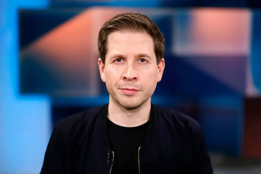 Kevin Kühnert in schwarzem Oberteil blickt lächelnd in die Kamera