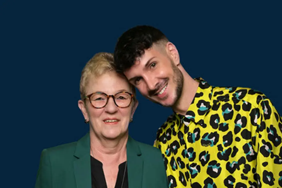 Kevin im gelb gemusterten Hemd und seine Mama Michaela Schäfer mit Brille und grünem Blazer lächeln vor dunkelblauem Hintergrund.