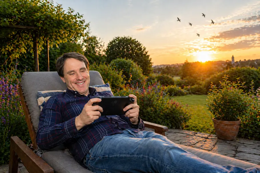 Aufmacher PS6 Portable Redakteur Joris Ujen liegt auf Gartenliege im Garten und spielt Handheld, hinter ihm geht die Sonne unter, Vögel fliegen