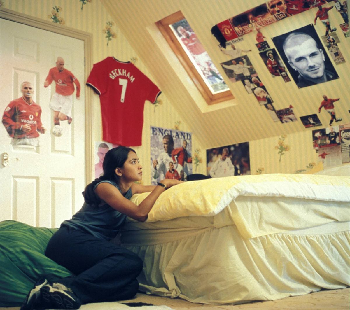 Parminder Nagra als fußballverrückte Jess in „Kick It Like Beckham“, umgeben von David-Beckham-Postern in ihrem Jugendzimmer. Szene aus Kick It Like Beckham: Jess (Parminder Nagra) liegt in ihrem mit Beckham-Postern dekorierten Zimmer.