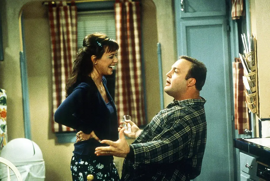 Leah Remini lächelt Kevin James an, der vor ihr kniet.