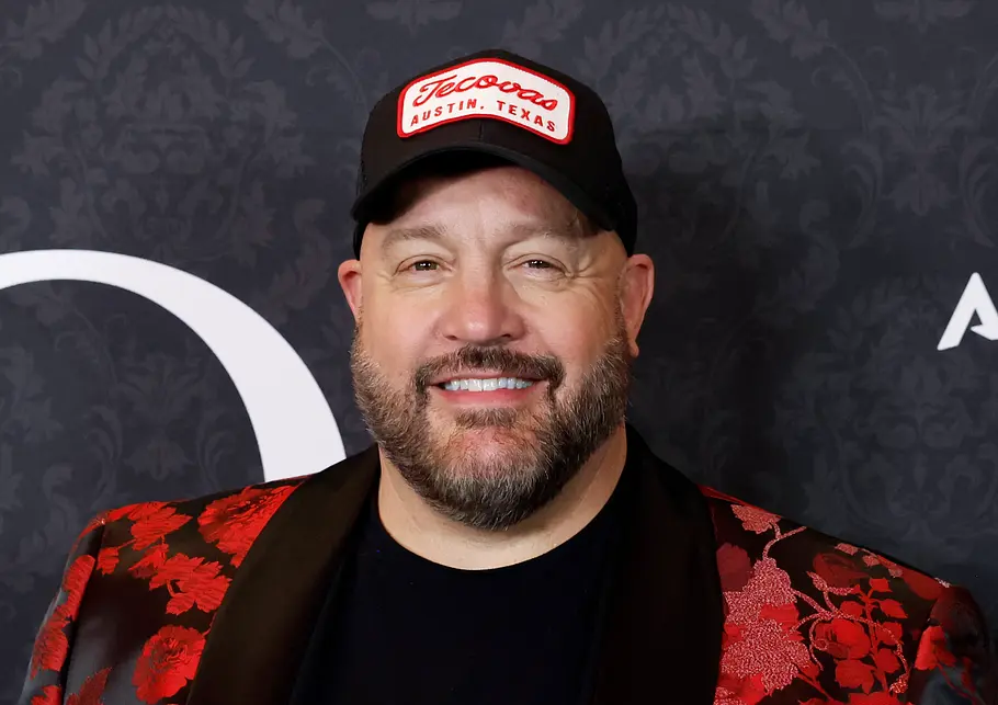 Kevin James lächelt vor einer Fotowand.