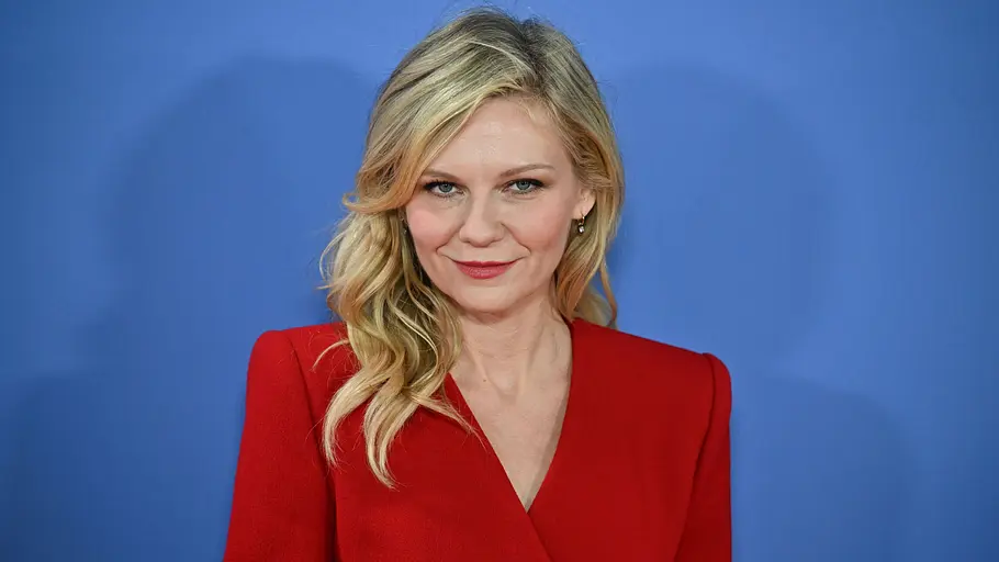Kirsten Dunst trägt auf dem roten Teppich einen roten Blazer und schaut direkt in die Kamera.