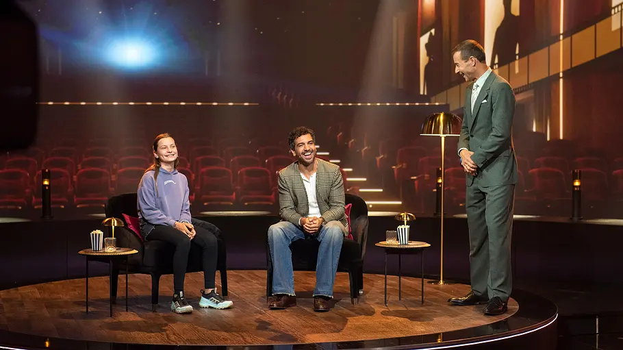 Elyas M’Barek bei „Klein gegen Groß“ 2026 Elyas M’Barek sitzt mit einer jungen Herausforderin im Kino-Set von „Klein gegen Groß“, während Kai Pflaume neben ihnen steht.
