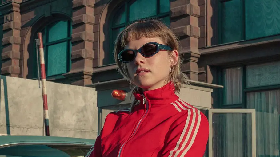 Jella Haase trägt eine Sonnenbrille und eine roten Sportanzug in „Kleo“.