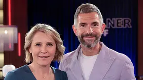 Zwei TV-Moderator:innen stehen nebeneinander im Studio und lächeln in die Kamera, im Hintergrund ist eine beleuchtete Talkshow-Kulisse zu sehen. - Foto: IMAGO / Future Image