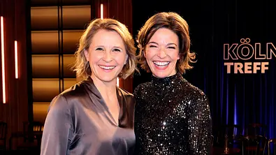 Zwei lachende Frauen stehen nebeneinander in einem Fernsehstudio. Im Hintergrund ist der Schriftzug „Kölner Treff“ zu sehen, die Studiobeleuchtung sorgt für eine warme Atmosphäre. - Foto: IMAGO / Future Image