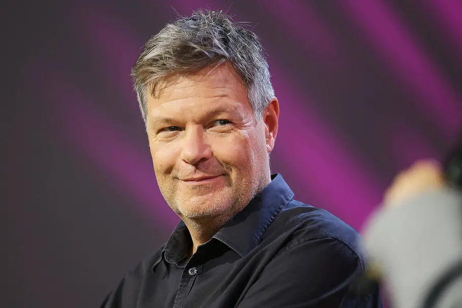 Robert Habeck trägt ein dunkles Hemd und lächelt leicht vor einem unscharfen violetten Hintergrund.