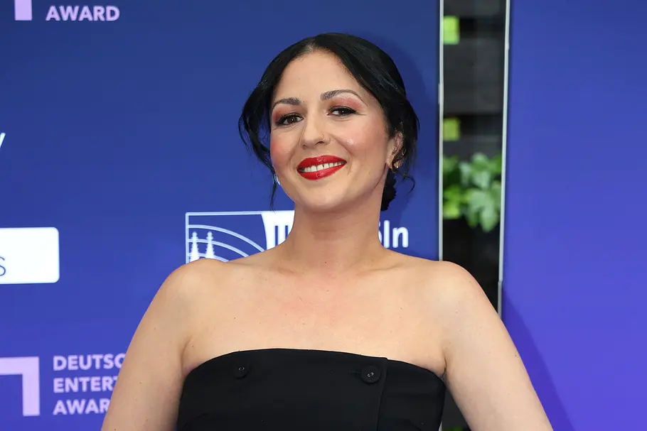 Tülin Sezgin lächelt in einem schwarzen, trägerlosen Kleid vor einer blauen Veranstaltungswand.