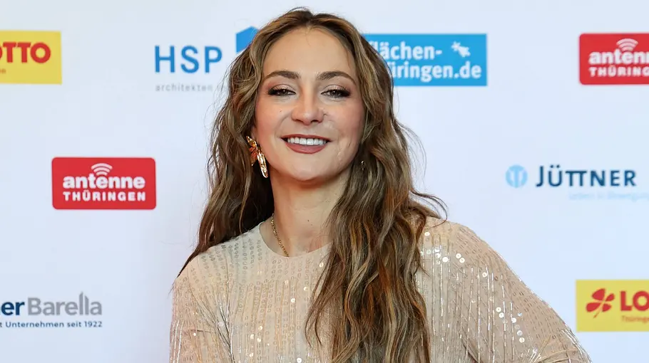 Kristina Vogel Let Dance Kristina Vogel sitzt lächelnd in einem Rollstuhl. Sie trägt ein helles Paillettenkleid vor einer Wand mit Sponsorenlogos.
