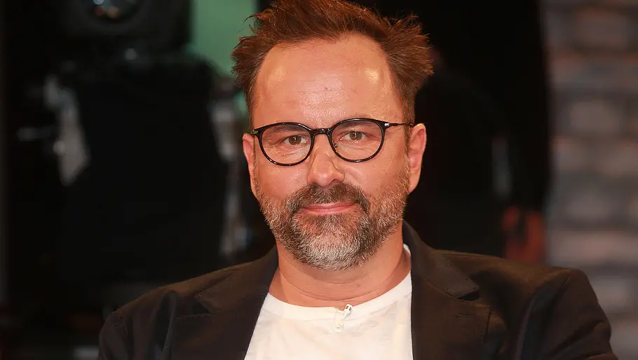Kurt Krömer zu Gast bei einer Talkshow 2022. Kurt Krömer schaut lächelnd in die Kamera.