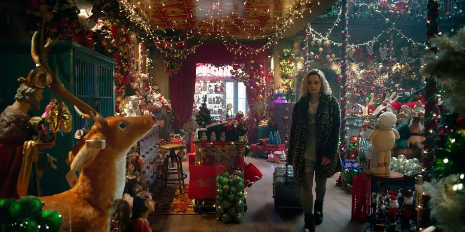 Last Christmas Emilia Clarke als Kate geht aus einem großen Weihnachtsdeko laden. Sie trägt einen Leo-Pelzmantel und zieht einen Koffer hinter sich her.