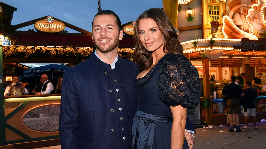 Laura Wontorra und Riccardo Basile werden Eltern. Laura Wontorra und Riccardo Basile stehen vor beleuchteten Bier- und Essensständen.